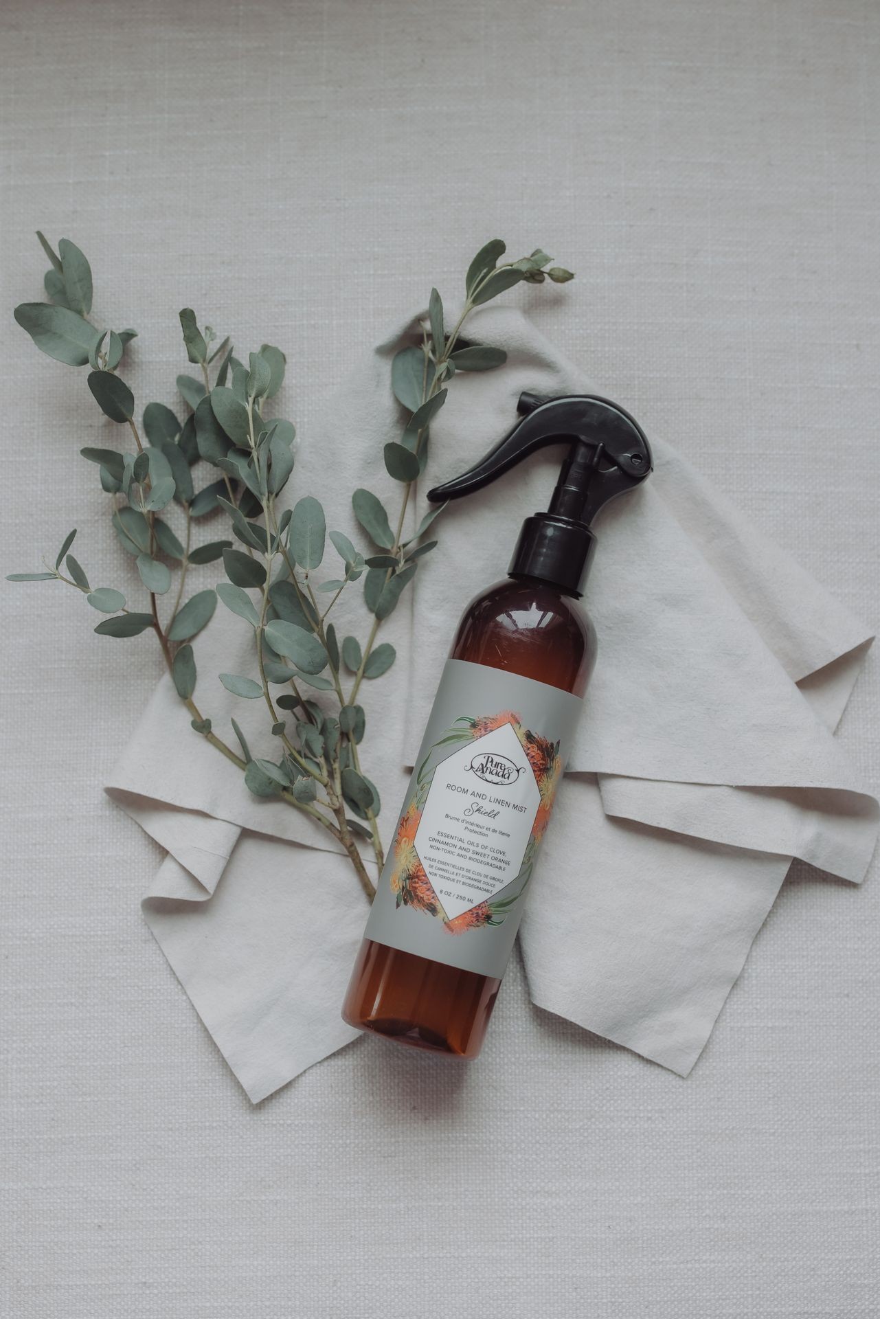 Bottle of room and linen mist spray placed on linen cloth with some eucalyptus leaves for decoration.