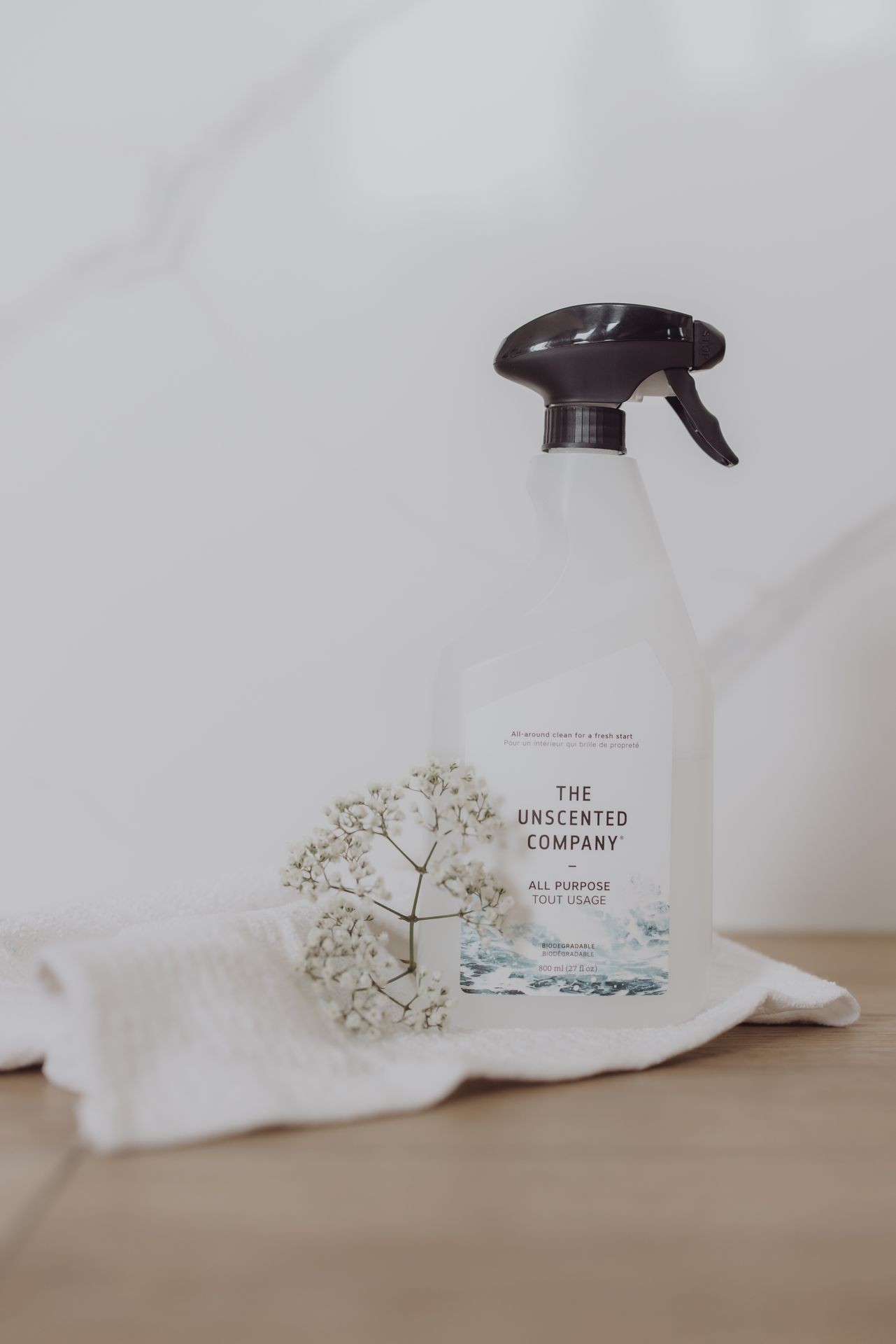 Spray bottle of all-purpose cleaner on a wooden surface with white flowers and a cloth.