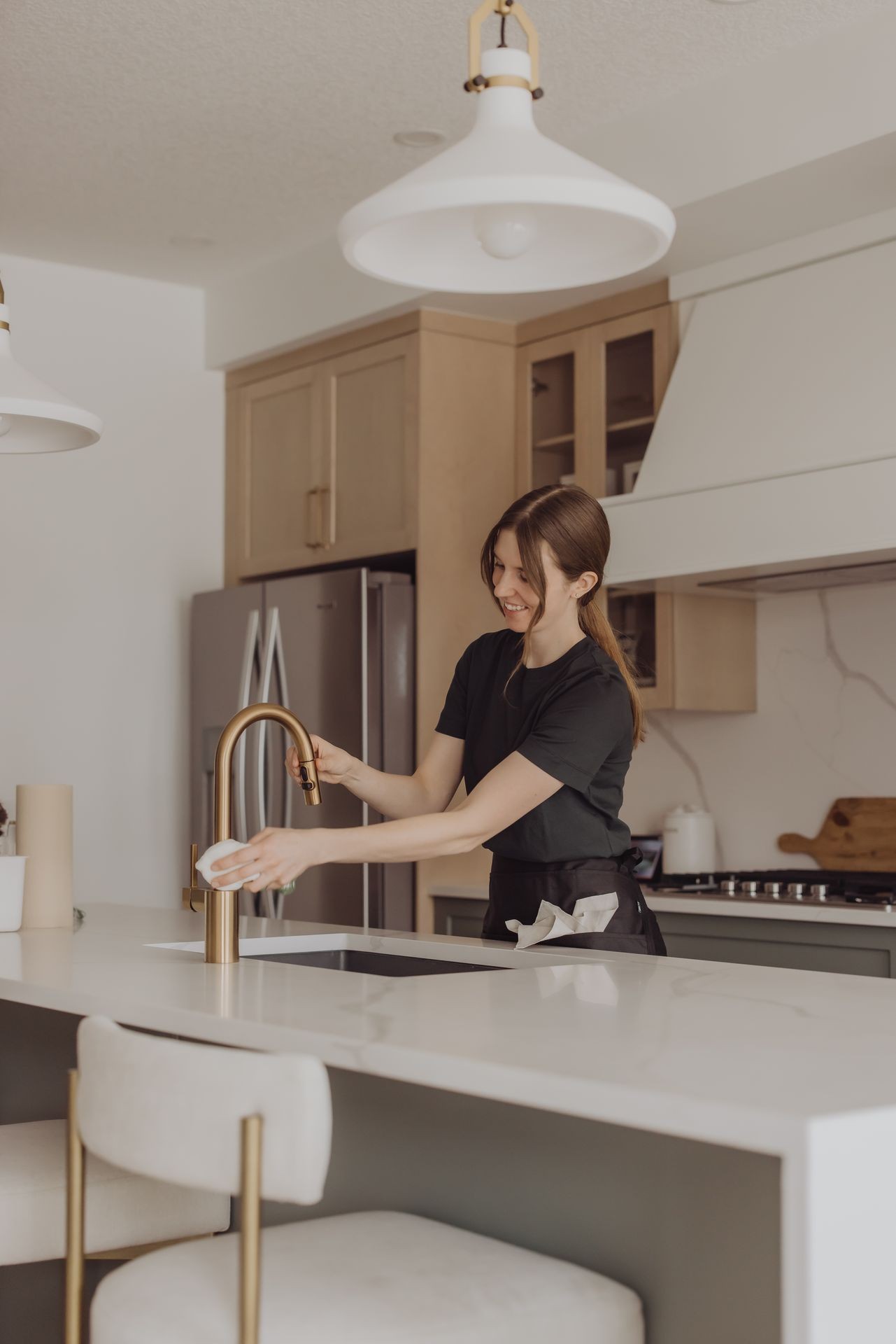 Woman cleaning a kitchen faucet with a cloth in a modern kitchen setting.