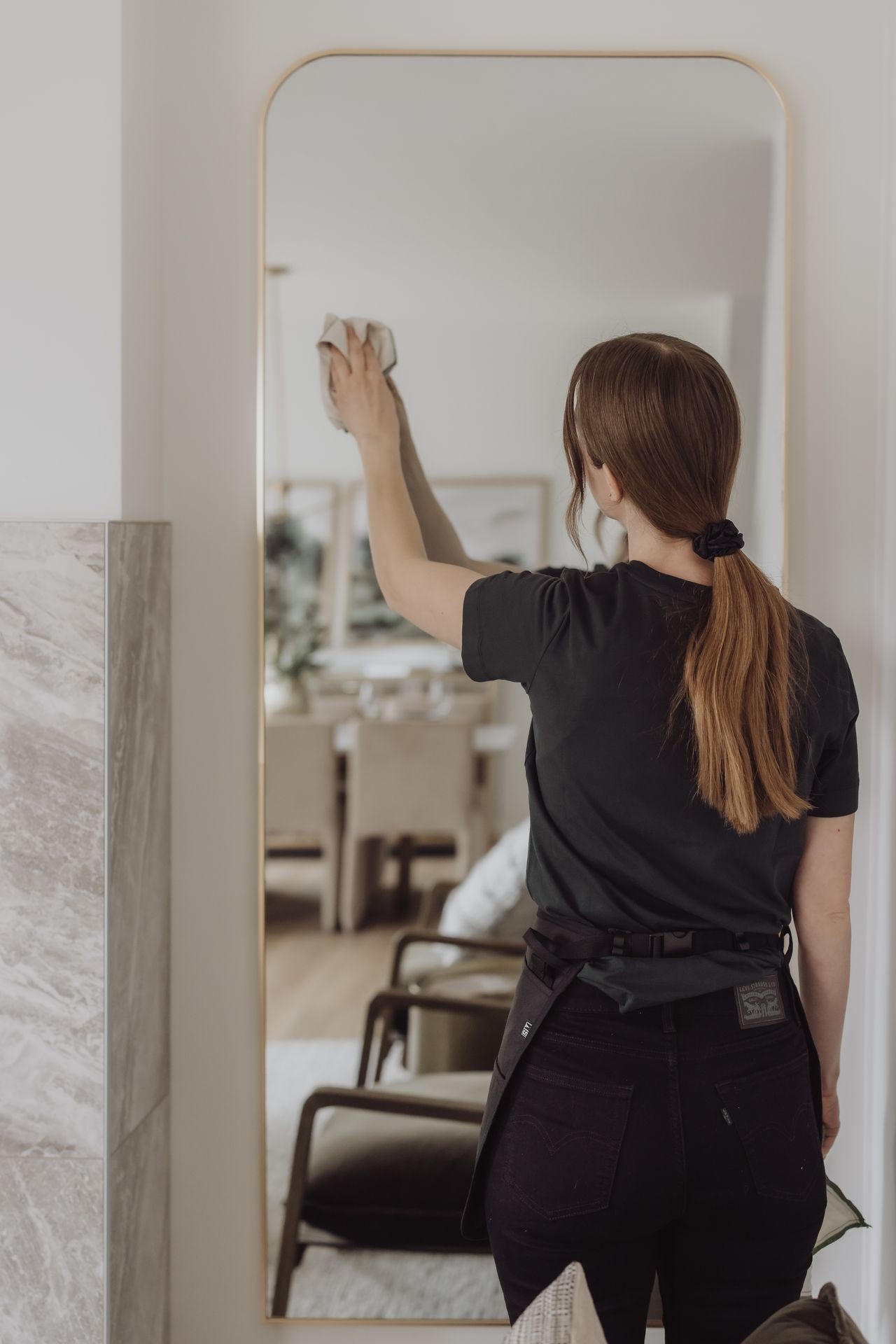 Person cleaning a large mirror with a cloth, standing in a modern living space.